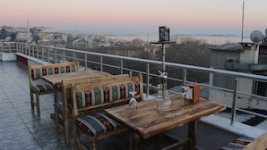 Una mesa de madera con bancos en un balcón con vistas a un paisaje urbano con edificios y una masa de agua.