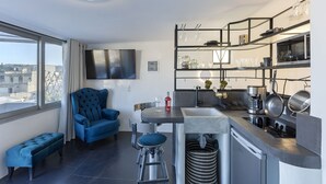 Une cuisine moderne équipée d’une cuisinière intégrée, d’une machine à café et d’un four à micro-ondes. On y trouve un tabouret de bar et une chaise bleue dans l’espace salon.
