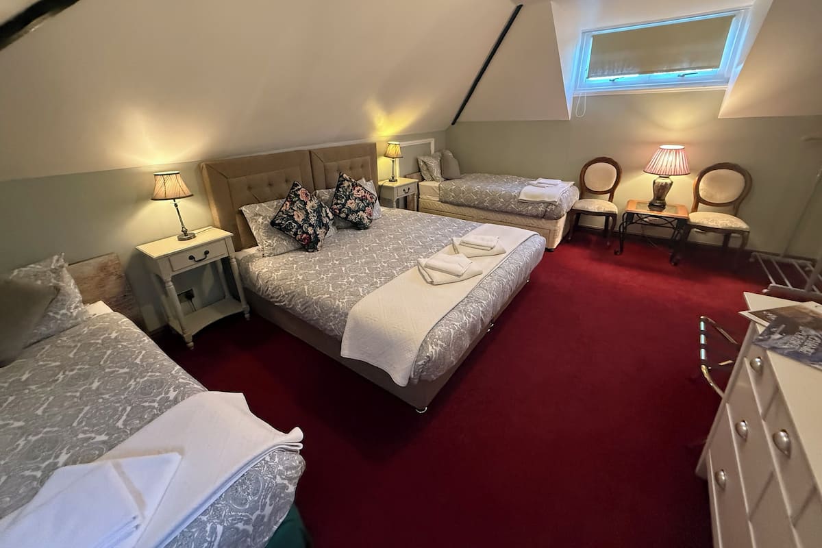 A bedroom with two beds, a desk, and a chair. There is a window with a view of the sky.