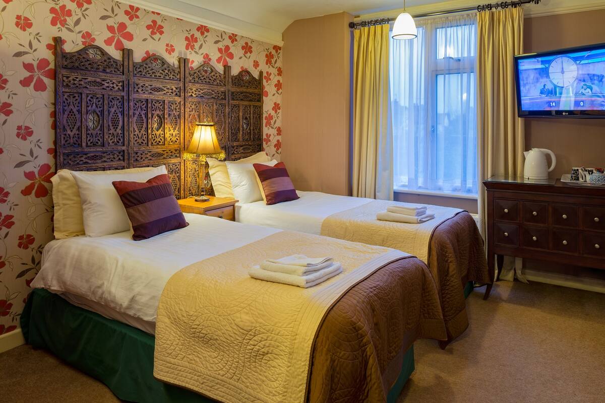 A hotel room with two beds, a wooden headboard, a TV, and a window with curtains.