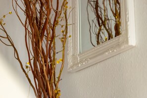 A white wall with a mirror reflecting branches and small yellow flowers. - Cambridge Bed and Breakfast (Cambridge)