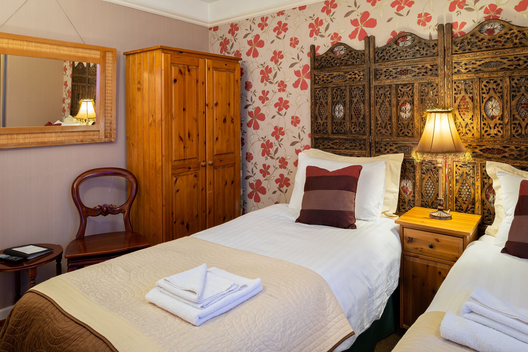 Una habitación de hotel con una cama grande, un armario de madera, un espejo y un cabecero decorativo.