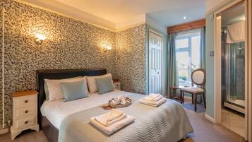 A bedroom with a large bed, two bedside tables, a chair, and a bathroom with a shower and a mirror.