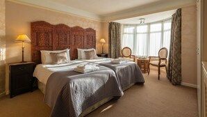 Ein Hotelzimmer mit einem großen Bett, zwei Nachttischen, einem Sessel und einem Fenster mit Vorhängen.