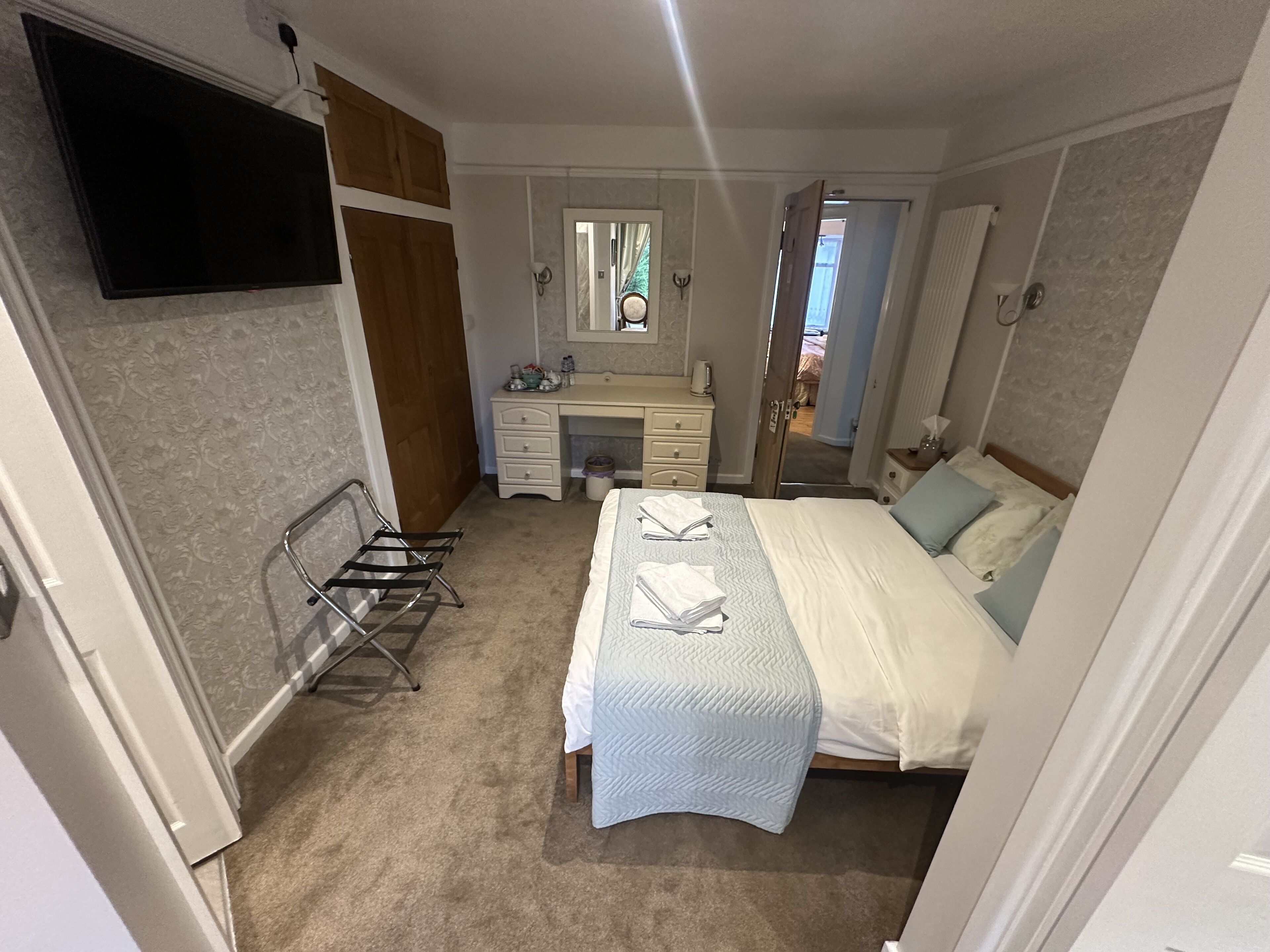 Un dormitorio con cama, tocador con espejo, cómoda y televisor montado en la pared.