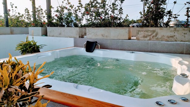 A hot tub with a wooden edge, surrounded by potted plants and a concrete wall.