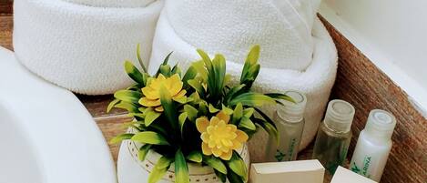 Un baño con una bañera blanca, una toalla blanca, una pequeña maceta con flores amarillas y dos botellas de champú.