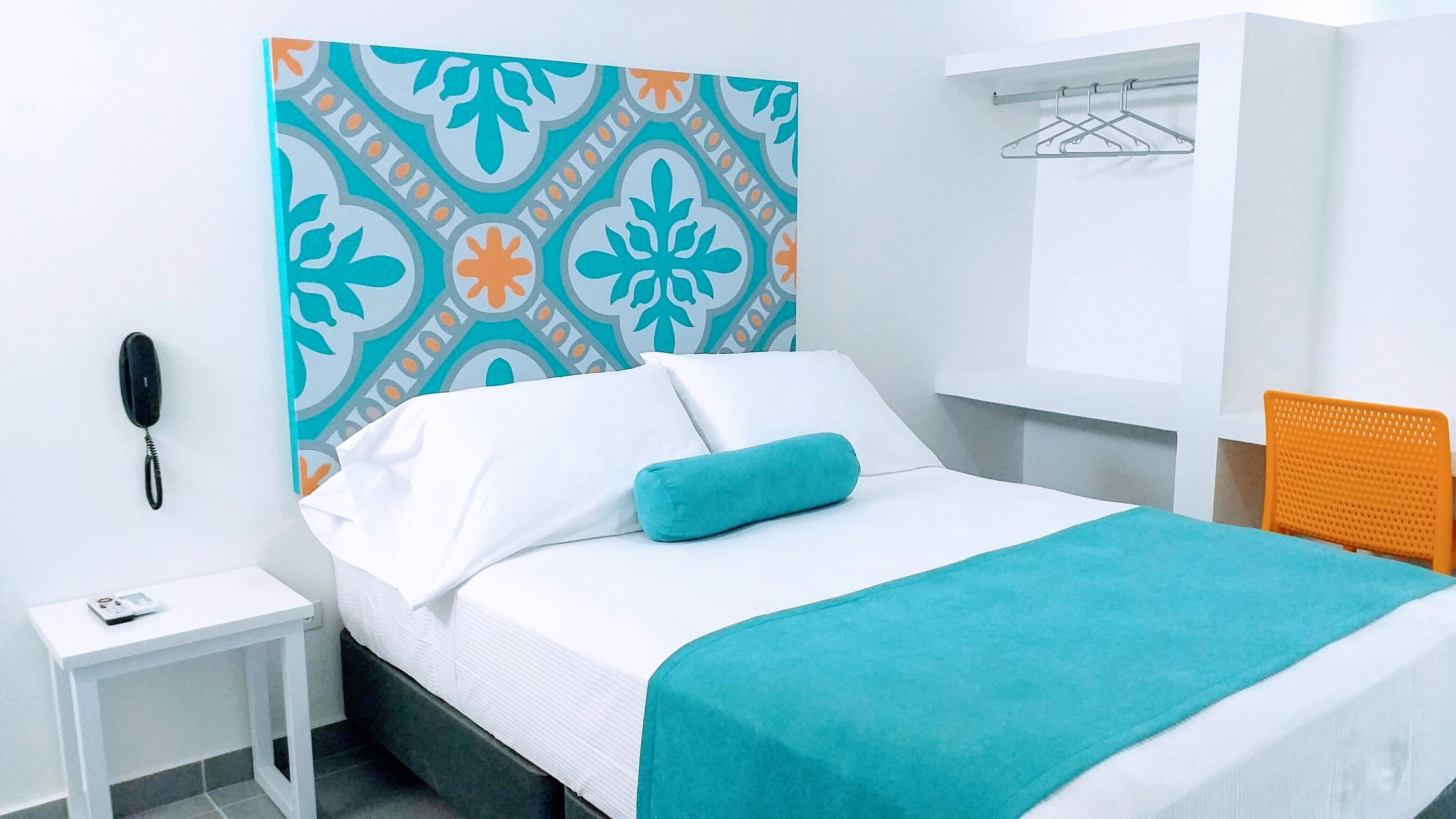 Een netjes ingerichte hotelkamer met een bed, nachtkastje, telefoon en wandrek.
