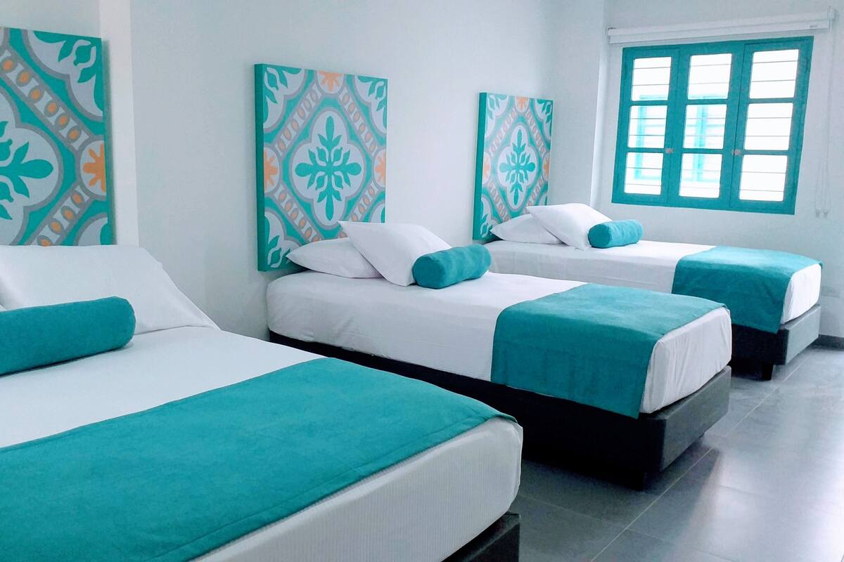 Ein Hotelzimmer mit zwei Betten, jeweils mit weißer Bettwäsche und Türkis-Akzenten. An den Wänden befinden sich dekorative Paneele mit geometrischen Mustern.