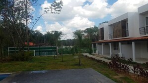 Uma casa moderna de dois andares com piscina em primeiro plano, cercada por um gramado bem cuidado e uma cerca verde.