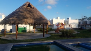 Um pavilhão com telhado de palha e uma piscina em primeiro plano.