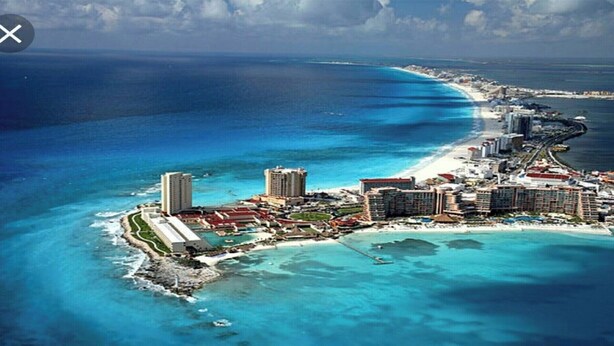 Vista aérea de uma área costeira com um resort, vários hotéis altos, uma praia e águas azul-claras.