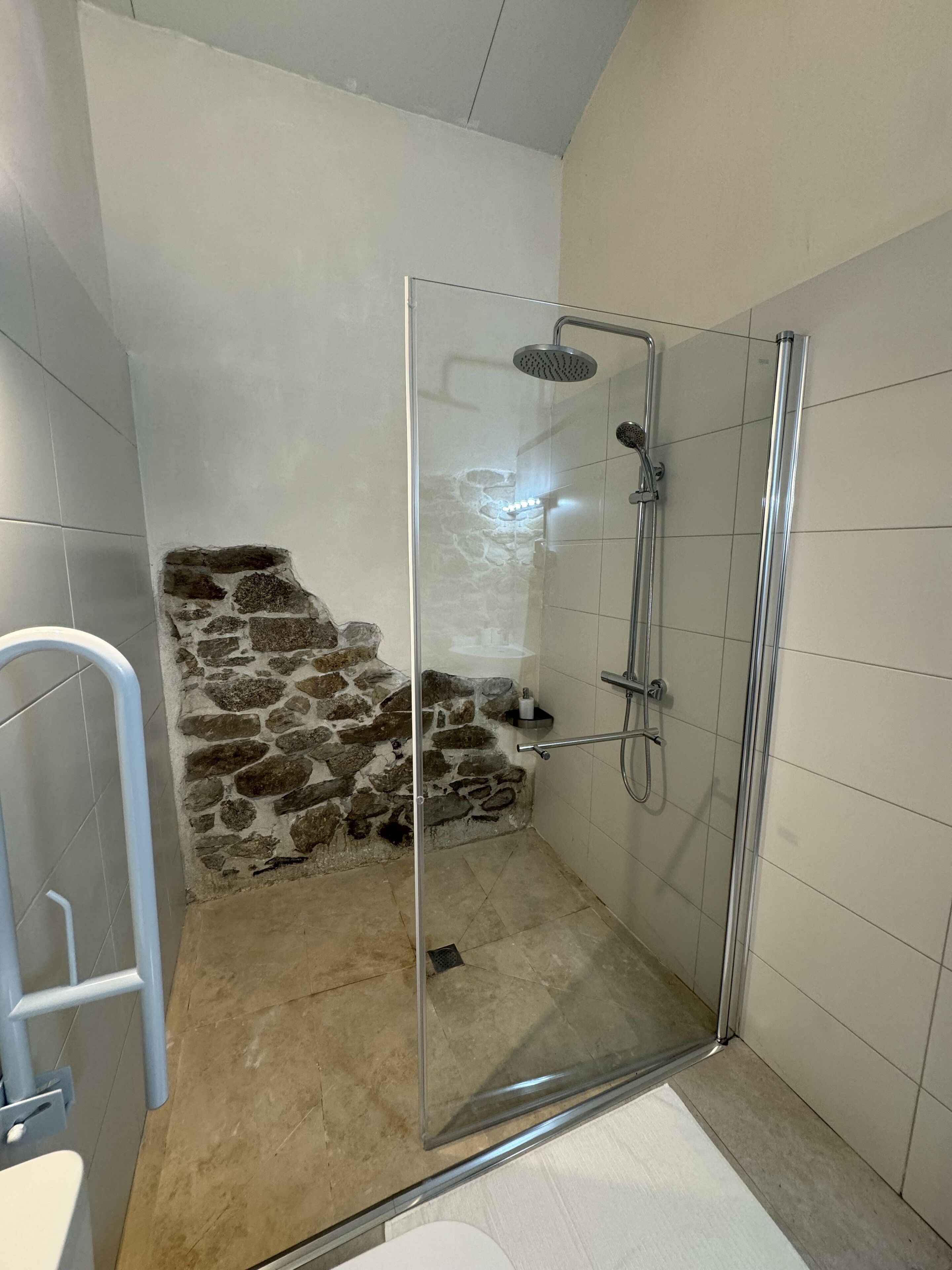 A shower area with a glass door, a stone wall, and a tiled floor.