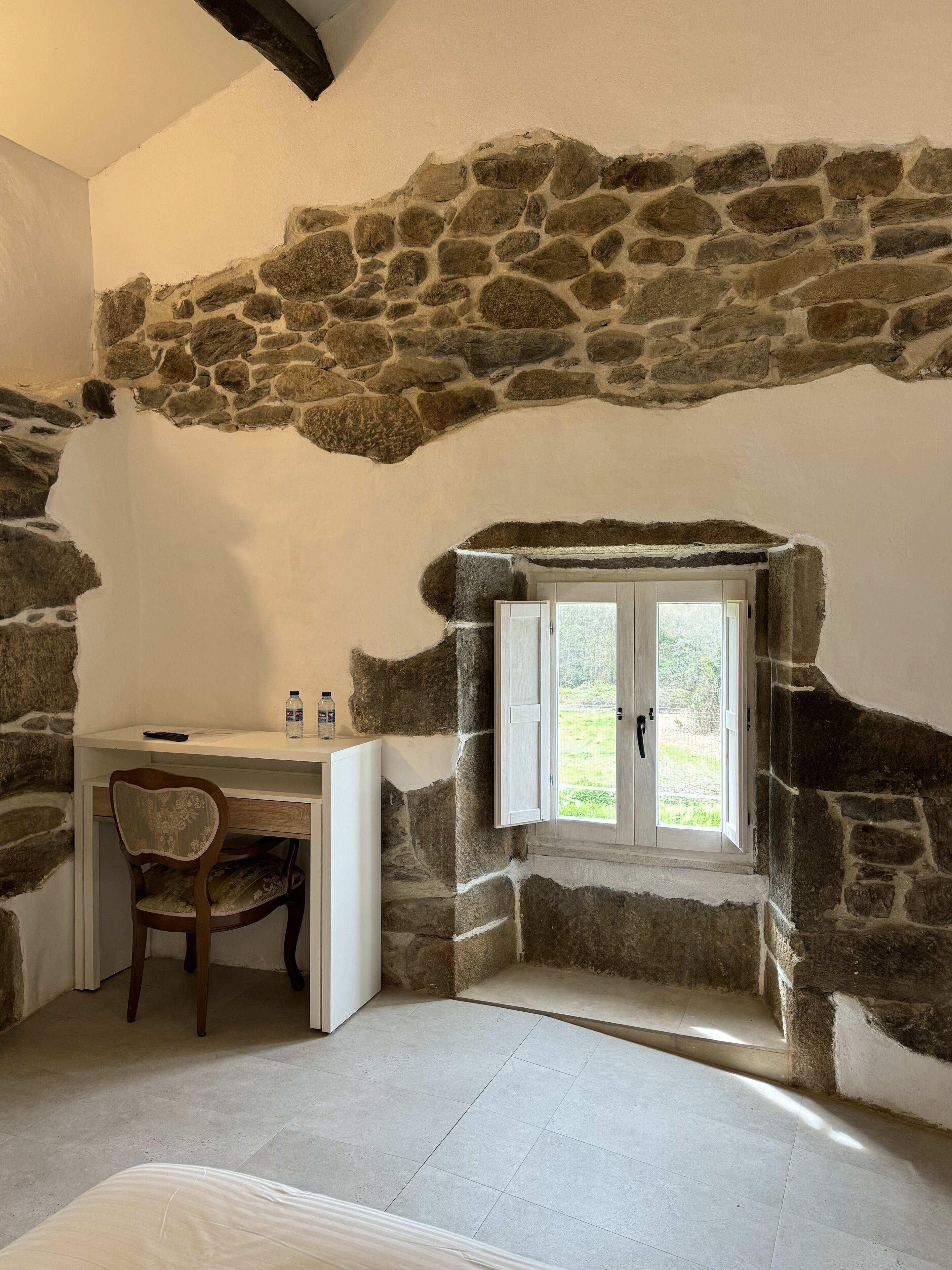 Ein Zimmer mit einer Steinwand, einem Schreibtisch mit Stuhl, einem Fenster und einem Bett.