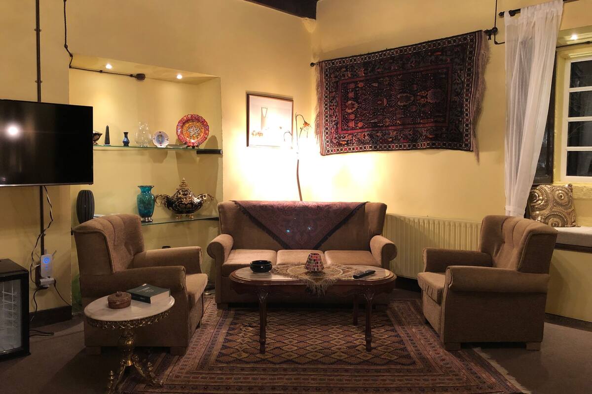 Una sala de estar con dos sillones, una mesita de centro, un televisor y un tapiz en la pared.