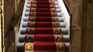 Una escalera con peldaños cubiertos de alfombra roja que lleva a una plataforma con un estante rojo que contiene varios objetos.