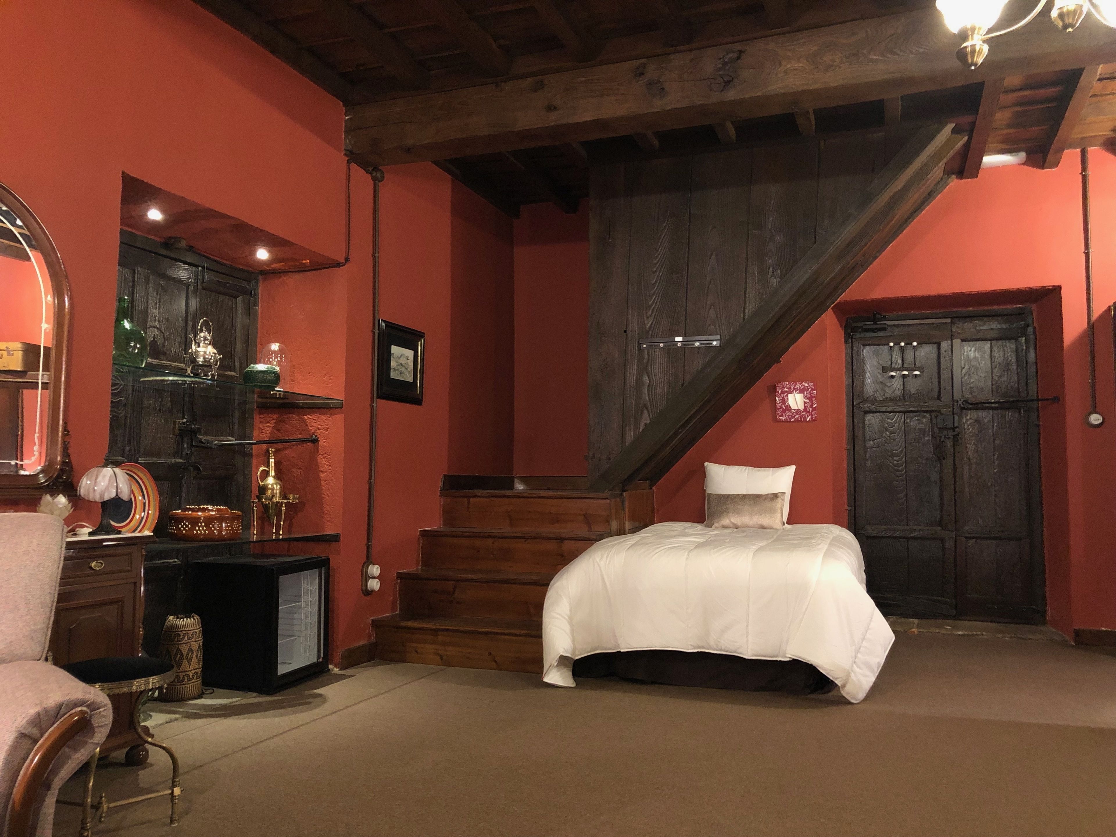 Un dormitorio con una cama, una silla, un aparador, un espejo y una escalera.