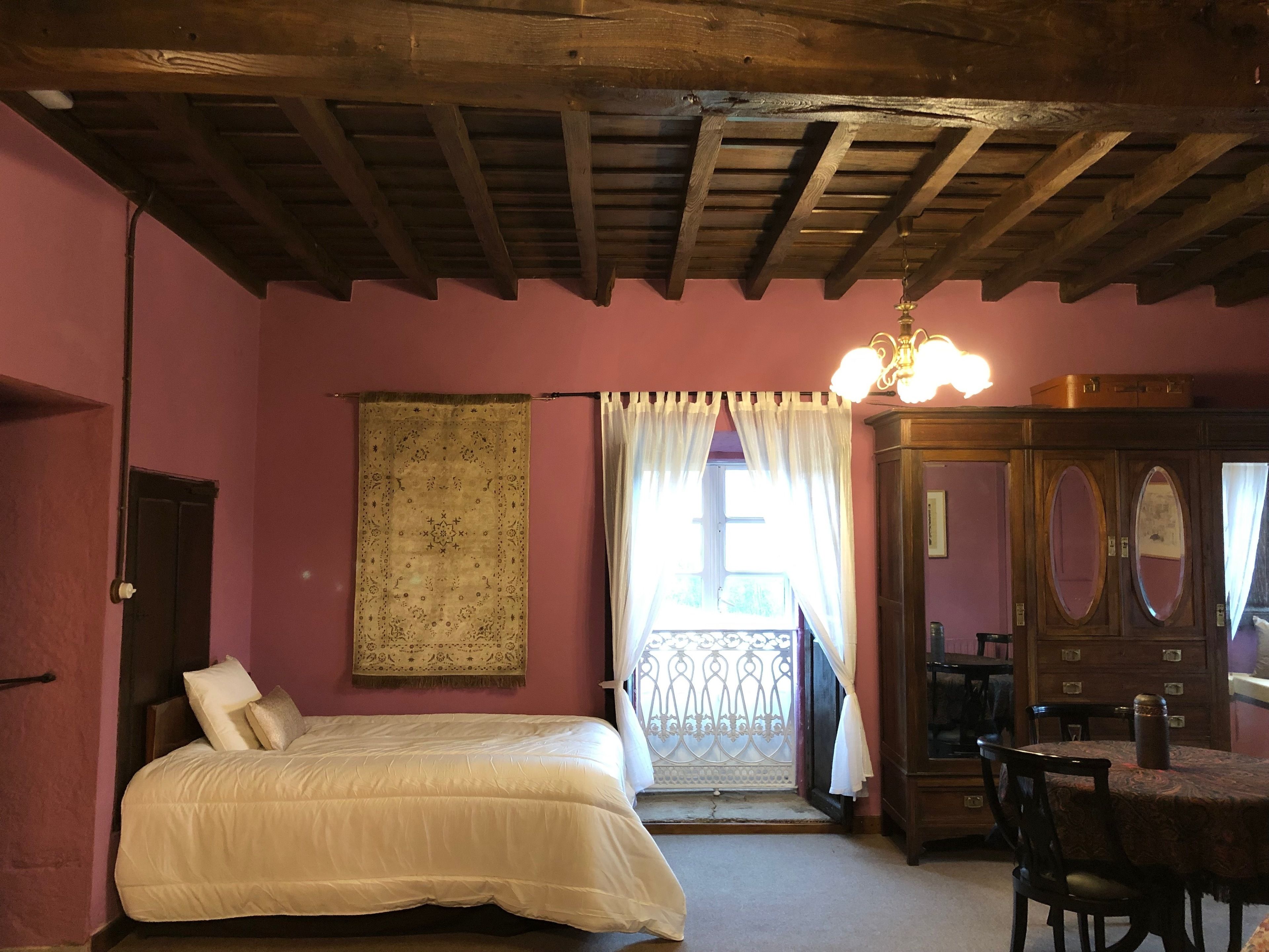 Ein Schlafzimmer mit Holzboden, einem Bett mit weißer Bettwäsche, einem gemusterten Teppich, einem Holzschrank und einem Tisch mit Stühlen.