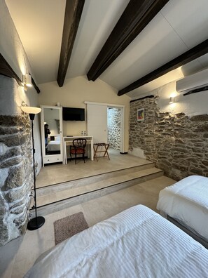 A bedroom with two beds, a desk, a chair, and a stone wall. - Pazo de Laia - Adults Only (Palas de Rei)