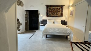 Un dormitorio con cama, un tapiz colgante y pared de piedra.