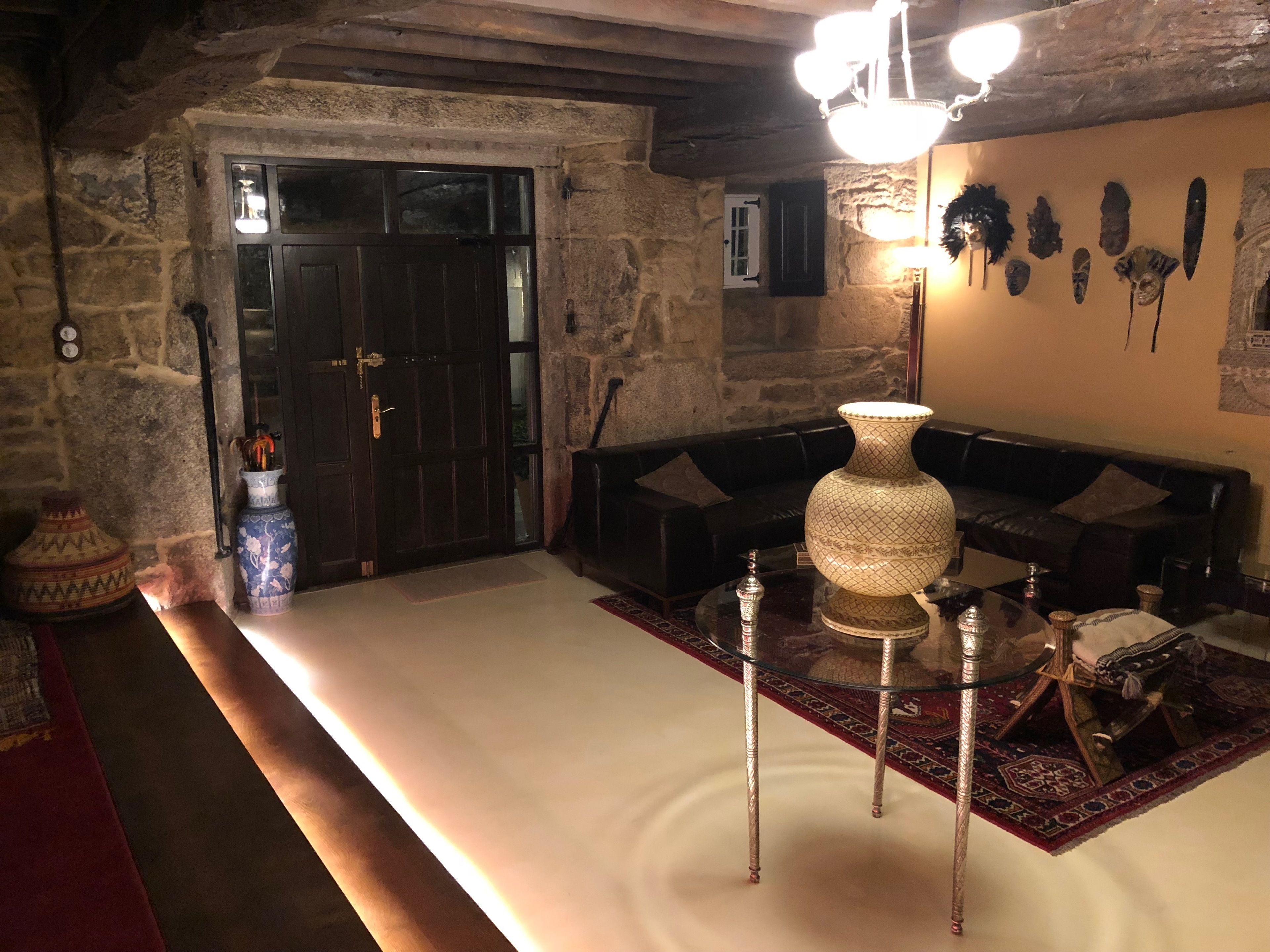 Una habitación acogedora con pared de piedra, puerta de madera, sofá de cuero negro, un jarrón decorativo grande y una alfombra tradicional.