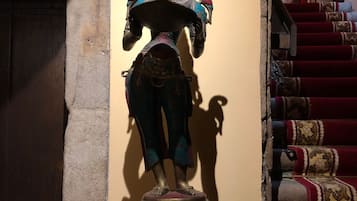 A statue of a deity with multiple arms, standing on a multi-tiered base, positioned against a wall with a staircase in the background.