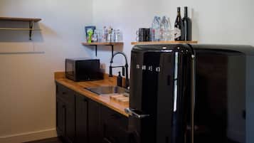 Uma cozinha compacta com geladeira preta, micro-ondas, pia e uma prateleira com água engarrafada e copos.