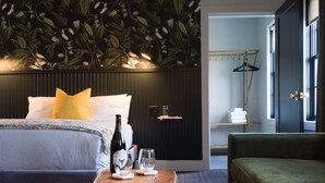 Una habitación de hotel moderna con una cama grande, una mesa de centro de madera, un sofá verde y una pared con un diseño de hojas.