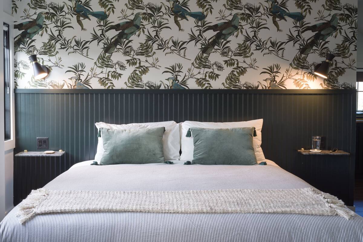 A neatly made bed with striped bedding, two pillows, and a decorative wall with a bird and plant pattern.