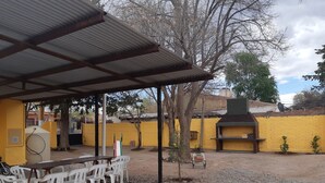 An outdoor patio with a covered seating area, a barbecue grill, and a yellow wall in the background. - Hotel El Nevado Malargüe (Malargüe)