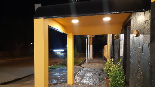 A hotel entrance with a wet tiled pathway leading to a covered area with a sign indicating the hotel name. - Hotel El Nevado Malargüe (Malargüe)