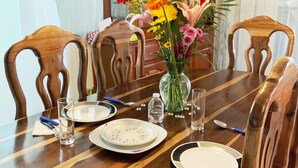 A dining table set for four with chairs, a vase of flowers, and a wooden cabinet in the background. - Casa Cuzamil (Cozumel)