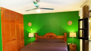 A bedroom with a wooden bed, green walls, a ceiling fan, and two wall-mounted lamps. - Casa Cuzamil (Cozumel)