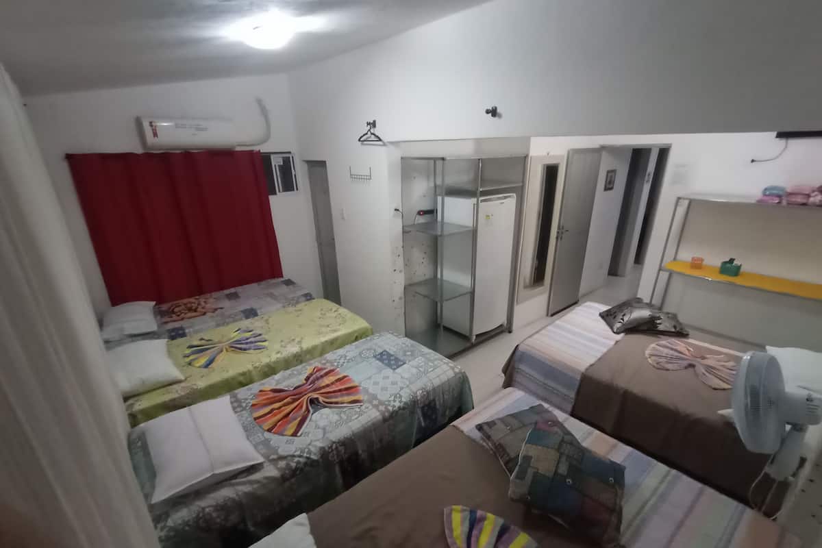 A dormitory room with two beds, a wardrobe, a mirror, and a fan.