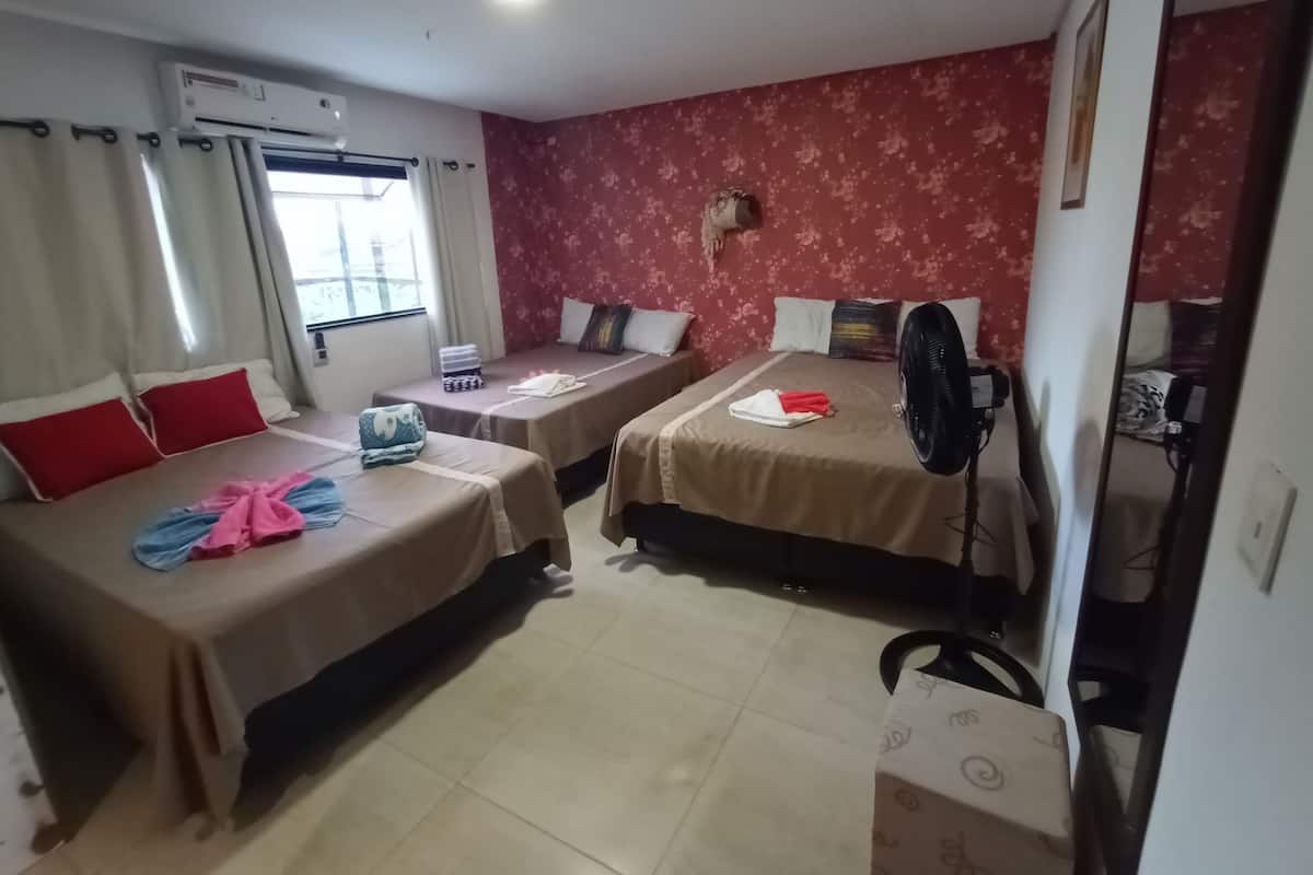 A hotel room with two beds, a window with curtains, a wall-mounted air conditioner, and a standing fan.