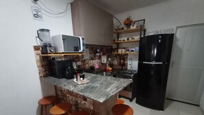 A kitchen with a central island, bar stools, a microwave, a coffee maker, and a refrigerator. - Lar Recife Olinda (Recife)