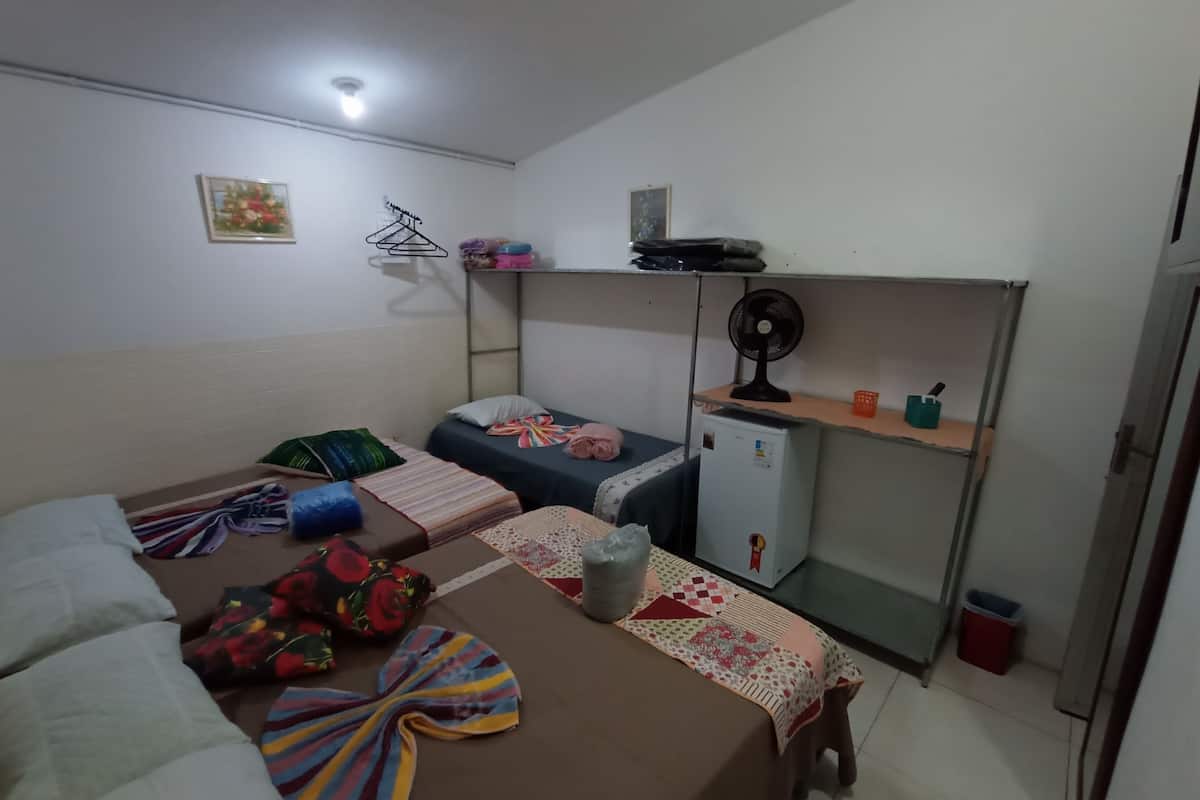 A small, compact room with two single beds, a small refrigerator, a fan, and a shelf with personal items.
