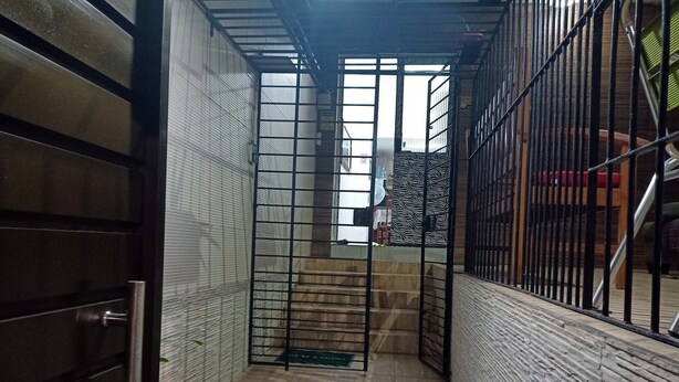 A narrow stairway with metal railings, a closed door on the left, and a patterned wall on the right. - Lar Recife Olinda (Recife)