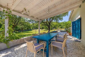 Une terrasse extérieure avec une table et des chaises, entourée de verdure et dotée d’un sol en pierre.