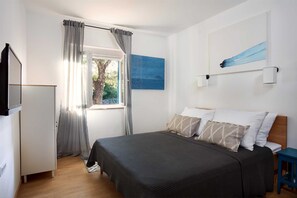 Une chambre à coucher avec un lit, une fenêtre avec des rideaux, un tableau accroché au mur et un téléviseur fixé au mur.