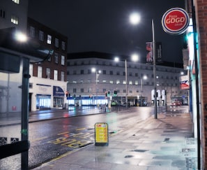 A nighttime street view with a pizza shop sign, a bus stop, and a building with multiple windows.