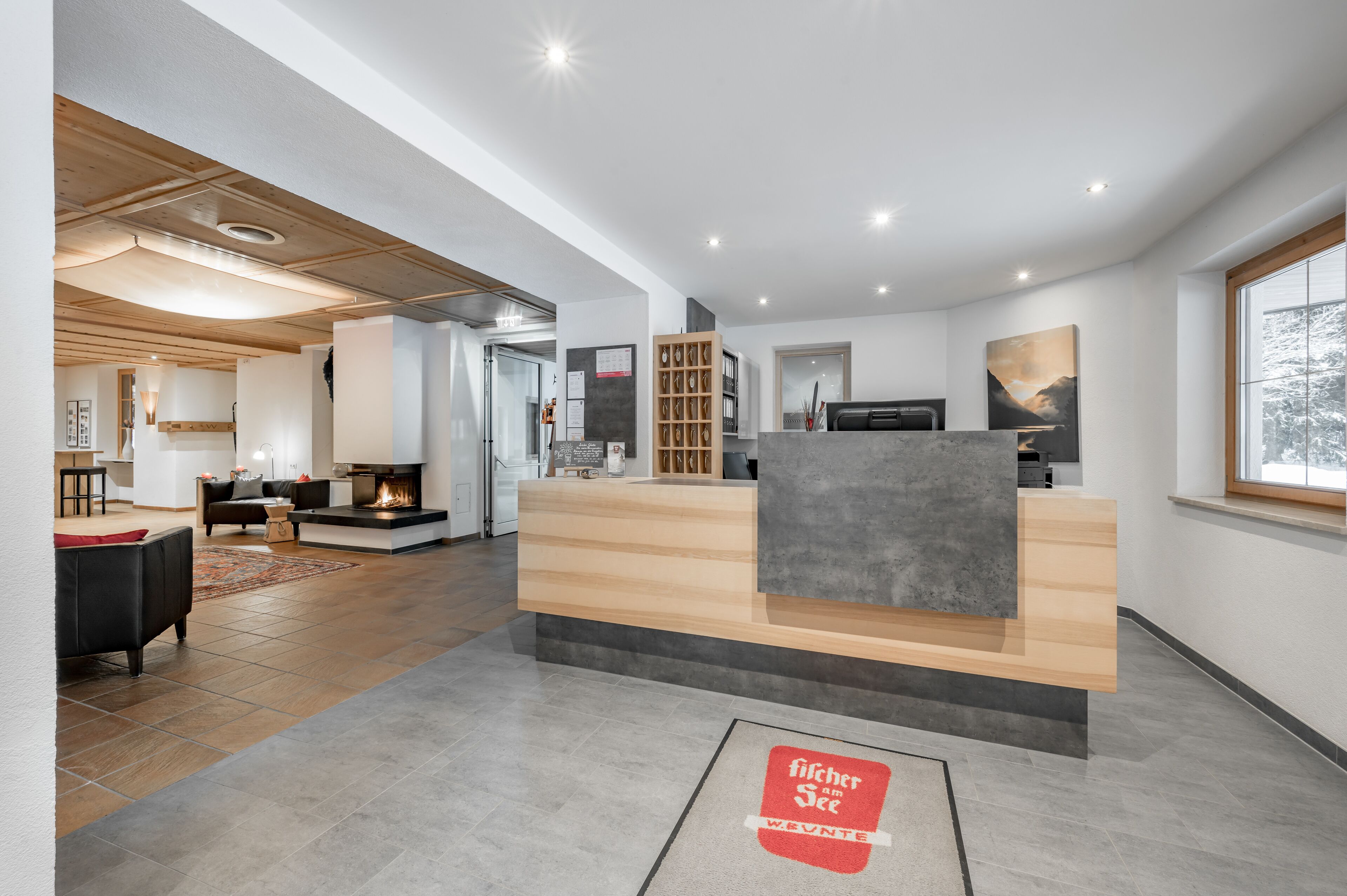 Un espace d’accueil moderne, doté d’un comptoir de réception en bois, d’une cheminée et offrant une vue sur l’extérieur.