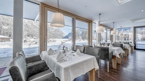 A restaurant with tables set for dining, large windows offering mountain views, and a modern interior design. - Hotel Fischer am See (Heiterwang)