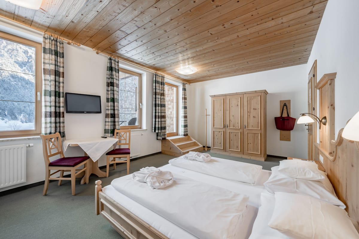 Hotellihuone, jossa on puukatto, sänky, työpöytä tuolilla, televisio ja näkymä lumiseen maisemaan.