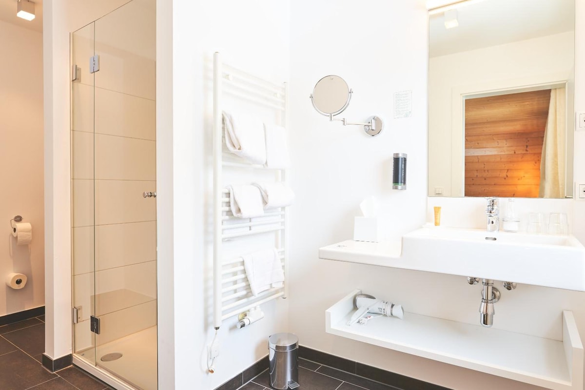 A modern bathroom with a glass shower enclosure, a white sink with a mirror, and a towel rack.