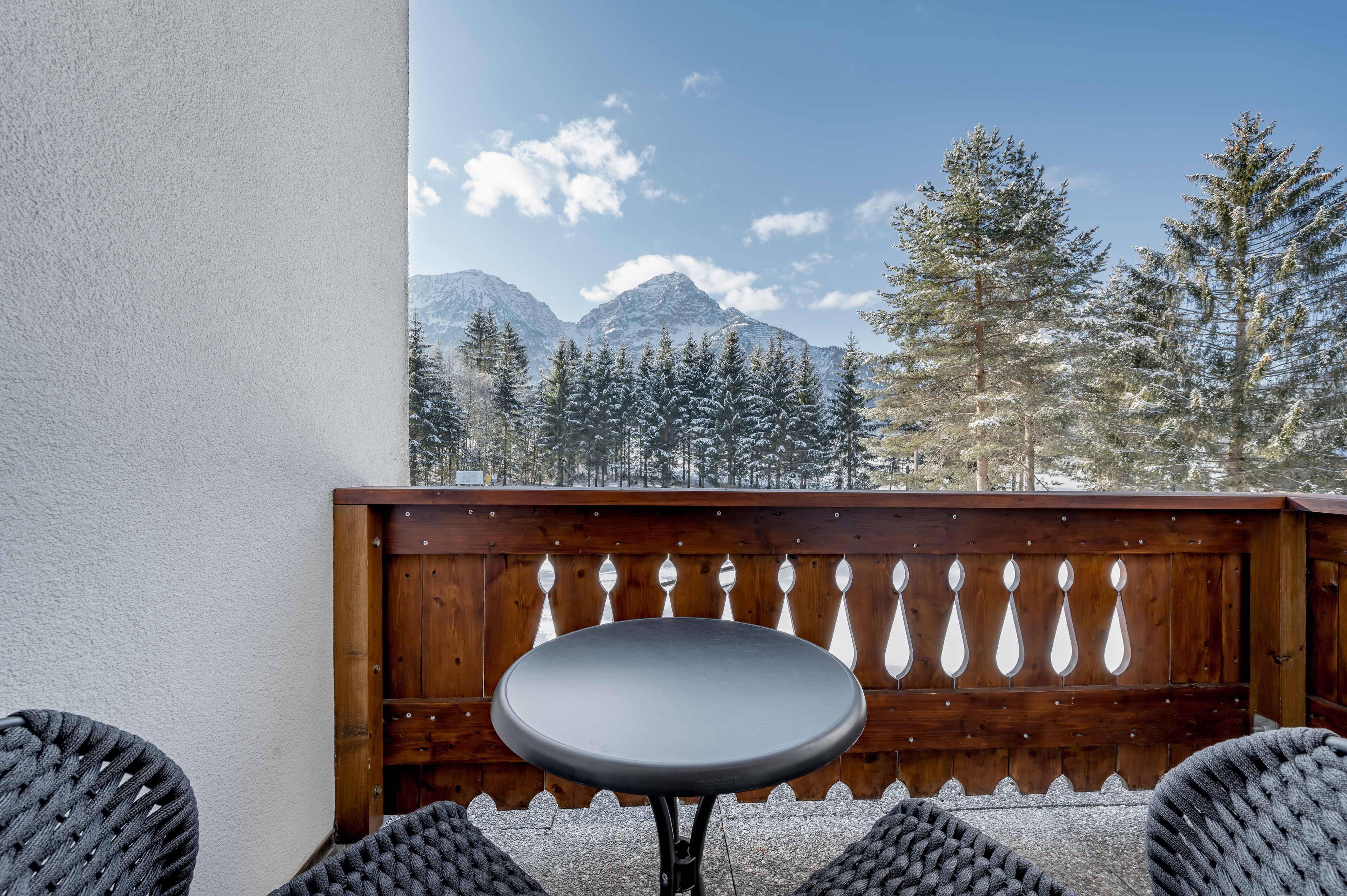 A balcony with a wooden fence, a round table, and wicker chairs.