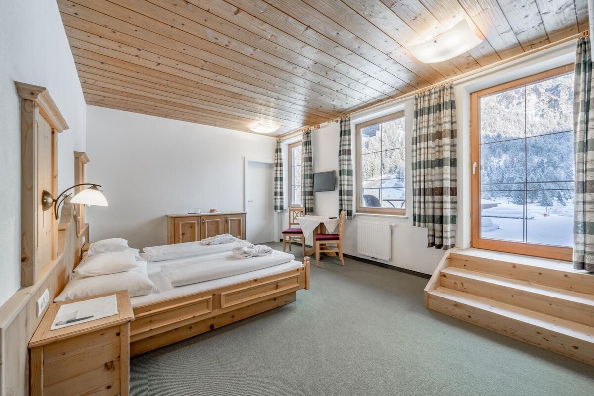 A room with a wooden ceiling, a bed, a desk, a chair, and a window with curtains.