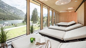 A room with large windows, wooden ceiling, and a view of a lake and mountains. - Hotel Fischer am See (Heiterwang)