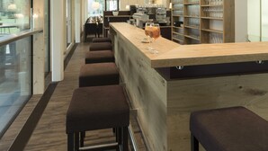 A modern bar area with a long counter, multiple stools, and pendant lighting. - Hotel Fischer am See (Heiterwang)