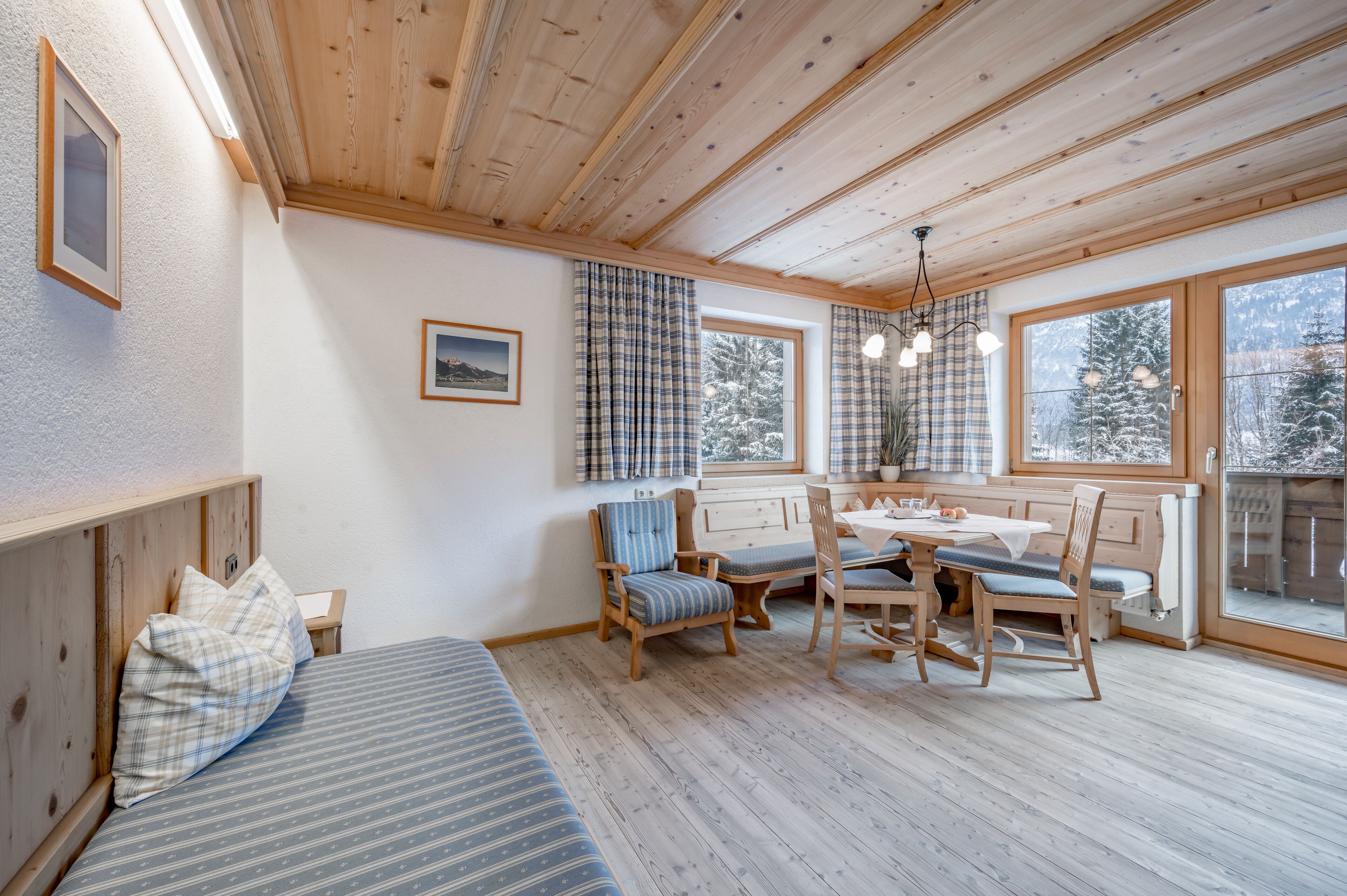 A cozy room with a bed, a dining table with chairs, and large windows with curtains.